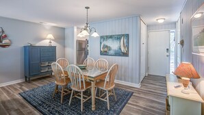 A dining area with a wooden table and chairs, a blue cabinet, a painting of sailboats, and a door leading to another room. - 89 Fairway Ln- 5 minute Walk to Beach (Hilton Head Island)