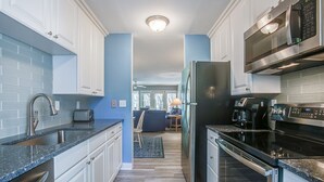 A modern kitchen with white cabinets, a black refrigerator, stainless steel appliances, and a blue accent wall. - 89 Fairway Ln- 5 minute Walk to Beach (Hilton Head Island)