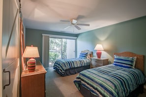 A bedroom with two beds, a ceiling fan, and a window with a view of greenery.