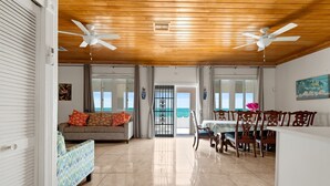 Amplia sala de estar con sofá, mesa de comedor, sillas, ventiladores de techo y vistas al exterior.