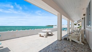Un espacio al aire libre cubierto con vista al mar, suelo de piedra y mobiliario exterior.
