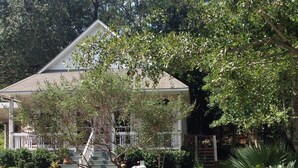 Una casa de dos pisos con porche delantero, rodeada de plantas variadas y un buzón.