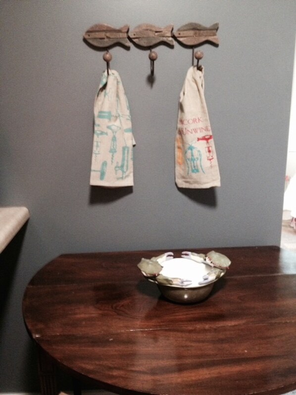 A wooden table with a metal bowl in the center, two cloths hanging on hooks above.