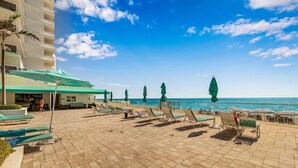 Eine Hotelterrasse direkt am Strand mit Liegestühlen, Sonnenschirmen und Blick aufs Meer.