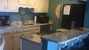 Una cocina con gabinetes blancos, encimera de granito, refrigerador y microondas.