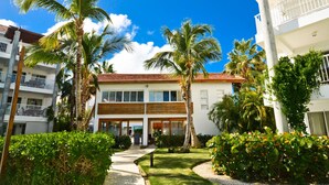 A two-story building with a red-tiled roof, surrounded by palm trees and lush greenery. - Oceanfront 2Bd/2Ba Penthouse Condo  (Bavaro)