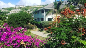 Una casa grande con balcón, rodeada de exuberante vegetación y flores coloridas.