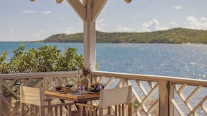 Una terraza de madera con una mesa lista para comer, con vistas a un cuerpo de agua y un paisaje montañoso.