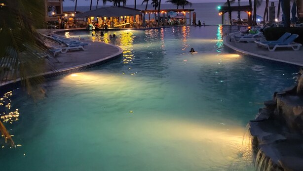 A pool area with lounge chairs and palm trees, surrounded by buildings with outdoor seating. - INFINITY BAY VACATION SALE! ULTRA Low Rates for our Low Season Dates! (West Bay Beach)