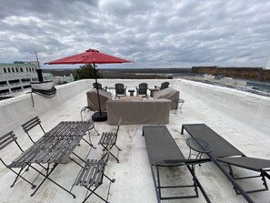 A rooftop patio with outdoor furniture, including a red umbrella, covered seating, and a view of the cityscape. - Gallery Loft Riverview Rooftop Terrace Elevator (Vicksburg)