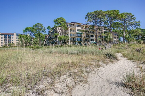 A beachfront hotel with multiple floors, outdoor balconies, and a sandy path leading to the beach.