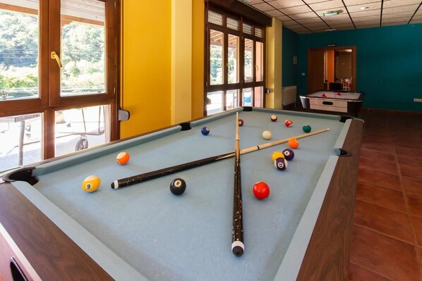 A pool table with balls and cues, a window with a view of greenery, and a teal wall. - Albergue Los Avellanos - Hostel (Pilona)