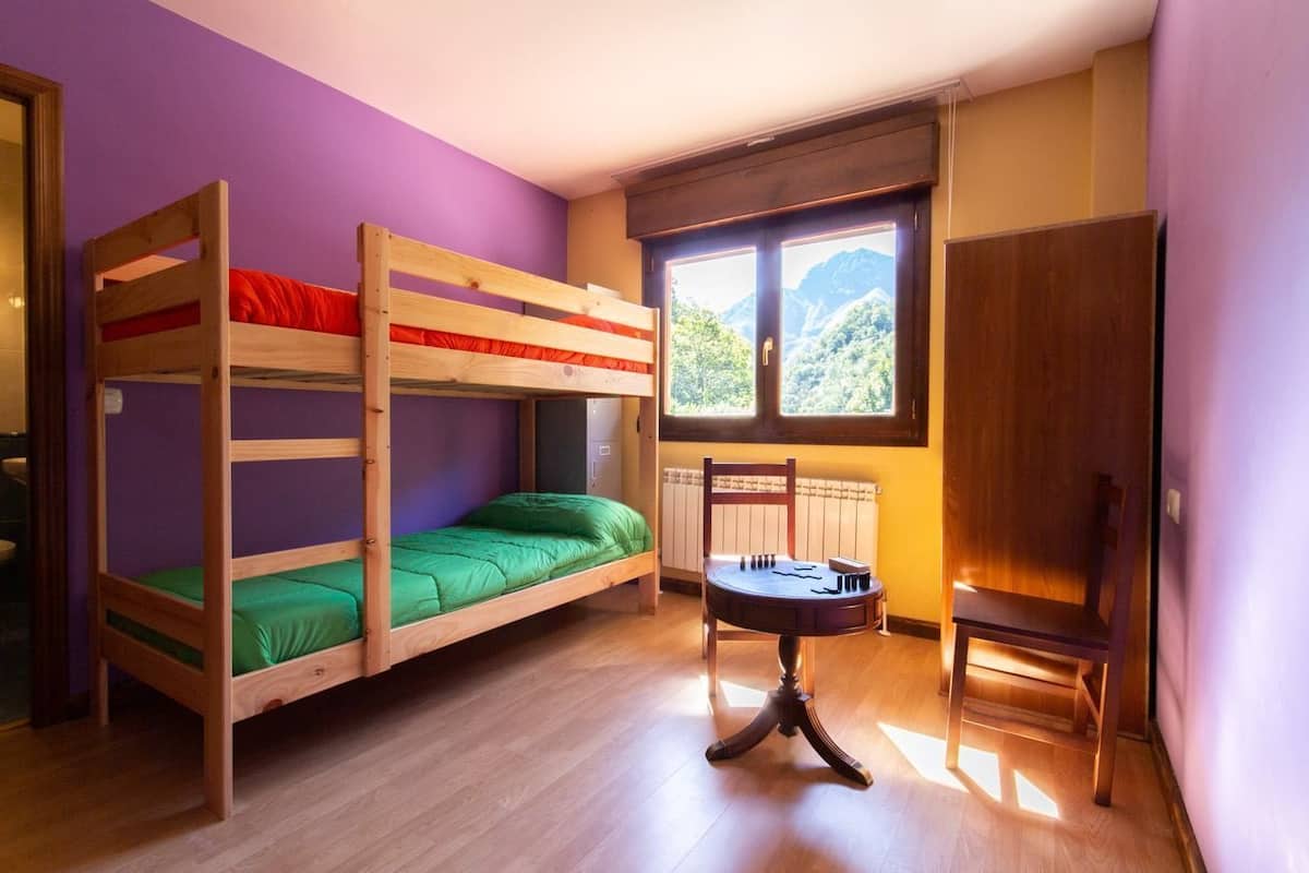 Une chambre avec un lit superposé, une fenêtre, un radiateur et une chaise en bois.