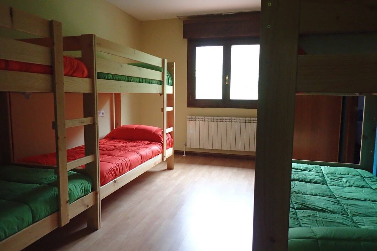 Une chambre de dortoir avec des lits superposés, un radiateur et une fenêtre avec des stores.