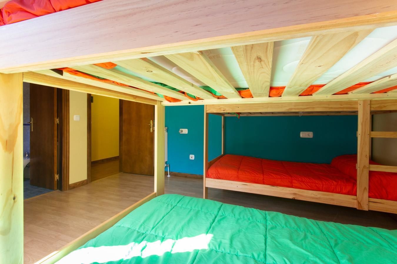 Una habitación con literas, vigas de madera y una pared color turquesa.