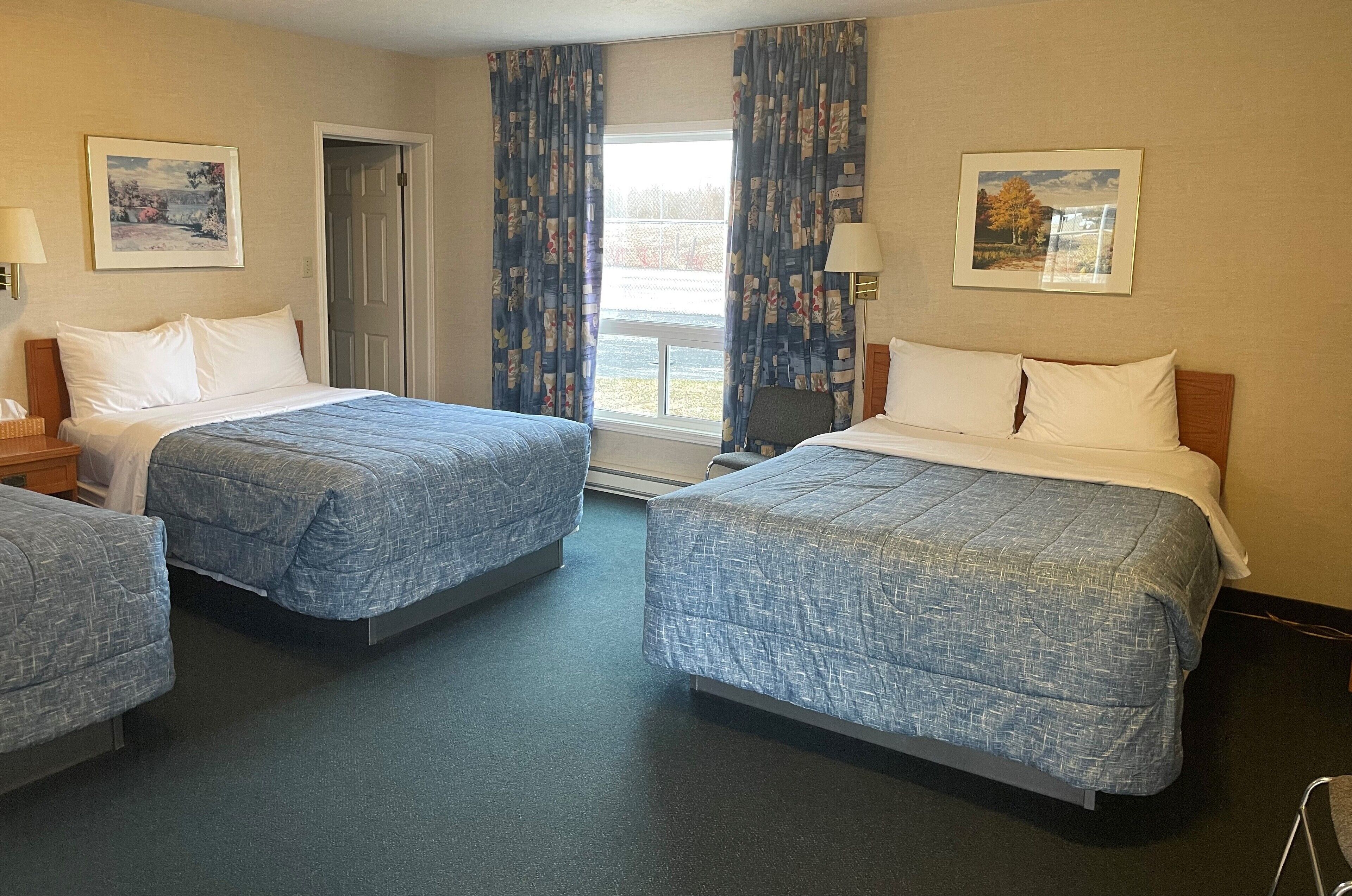 A hotel room with two beds, a chair, a desk, and a window with curtains.