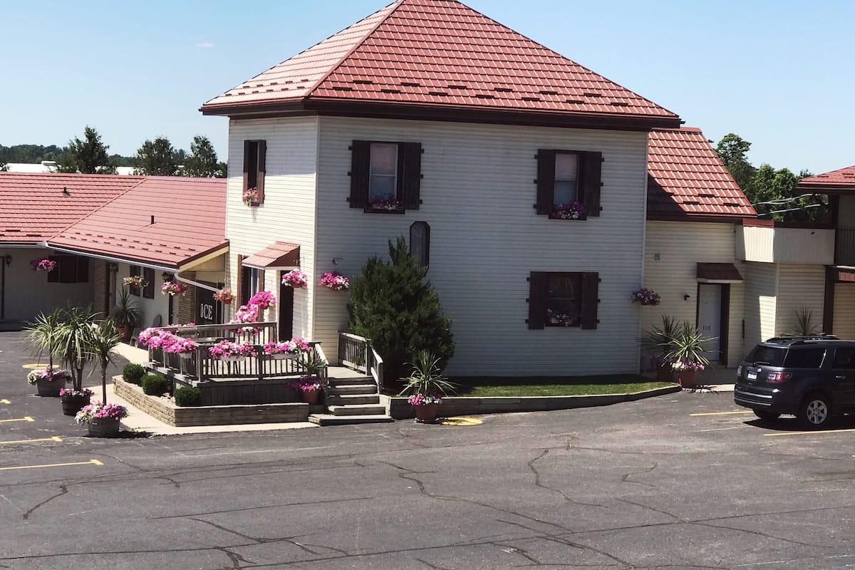 A two-story building with a red roof, a front porch with steps, and potted plants.