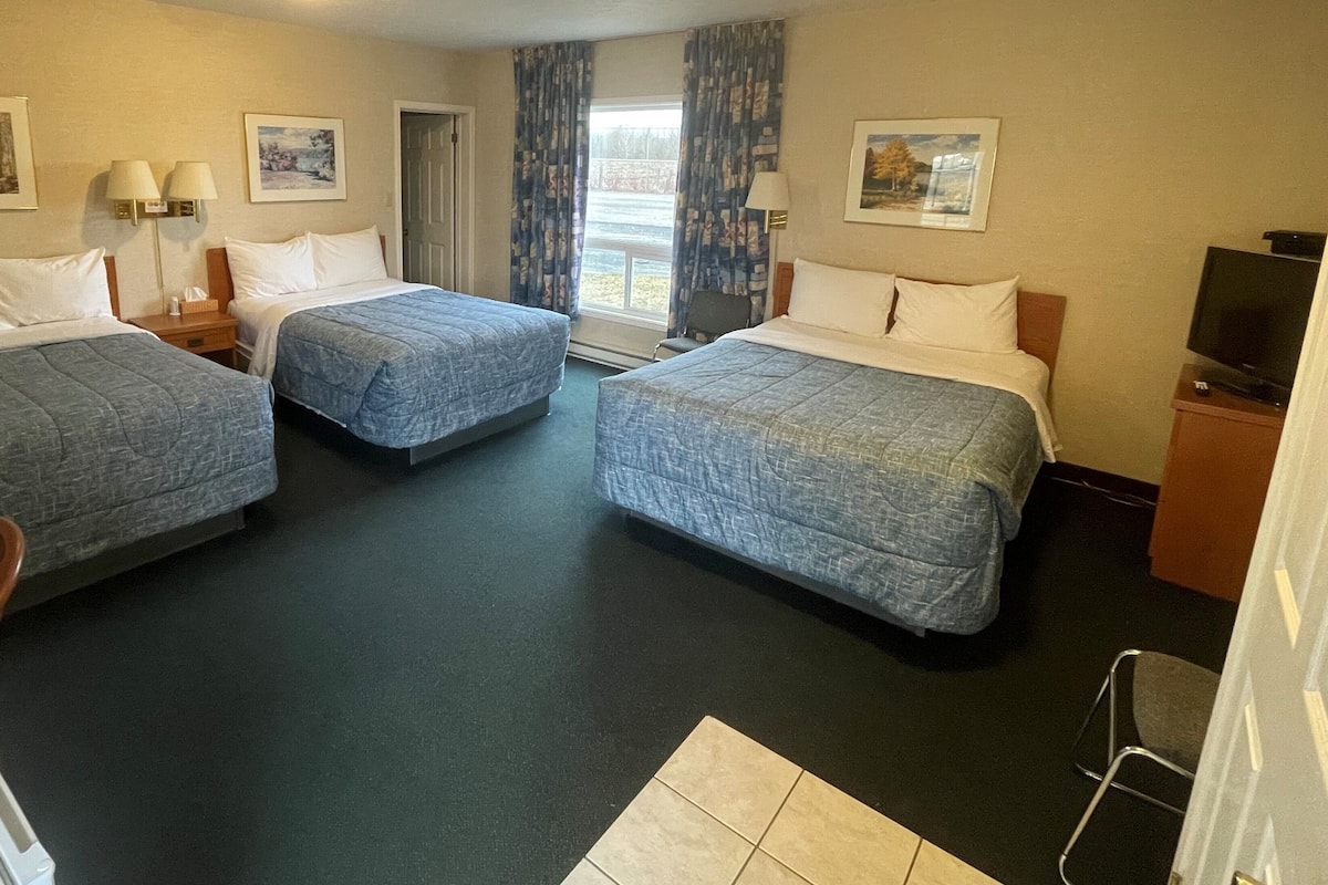 A hotel room with two beds, a desk, a chair, a TV, and a window with curtains.