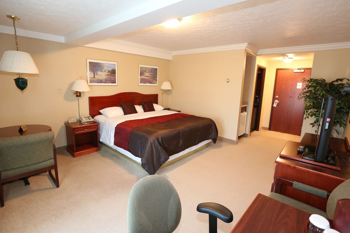 A hotel room with a bed, bedside tables, a desk, a chair, and a television.