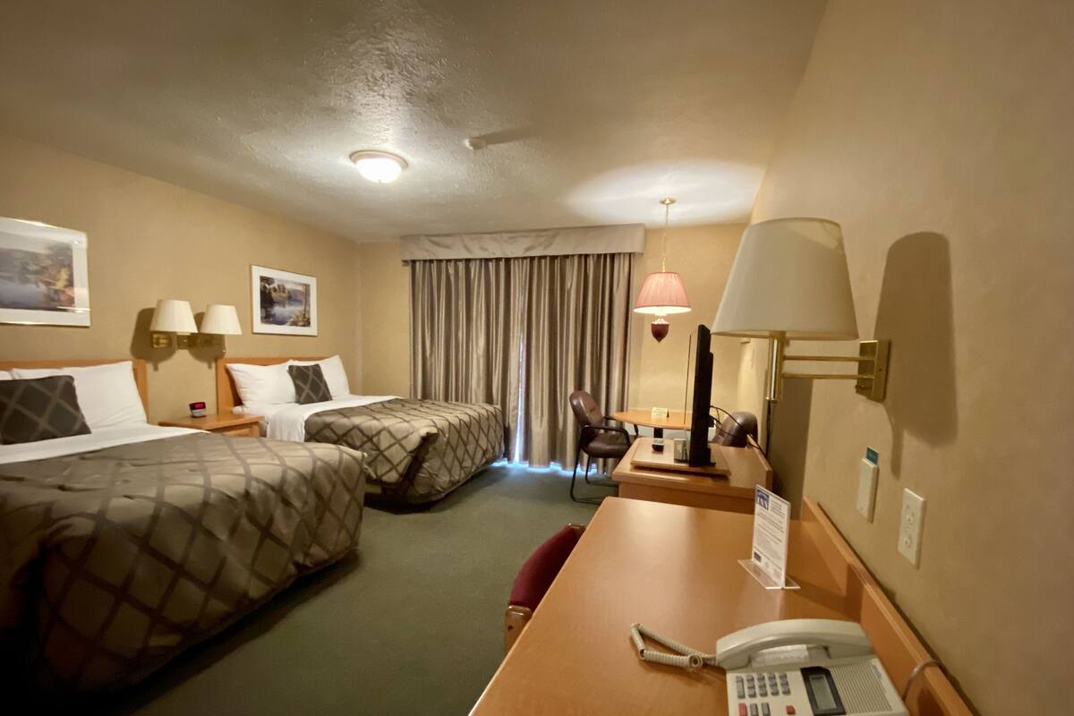 A hotel room with two beds, a desk with a telephone, a chair, and a desk lamp.