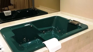 A bathroom with a large green bathtub, a mirror, and a sink.