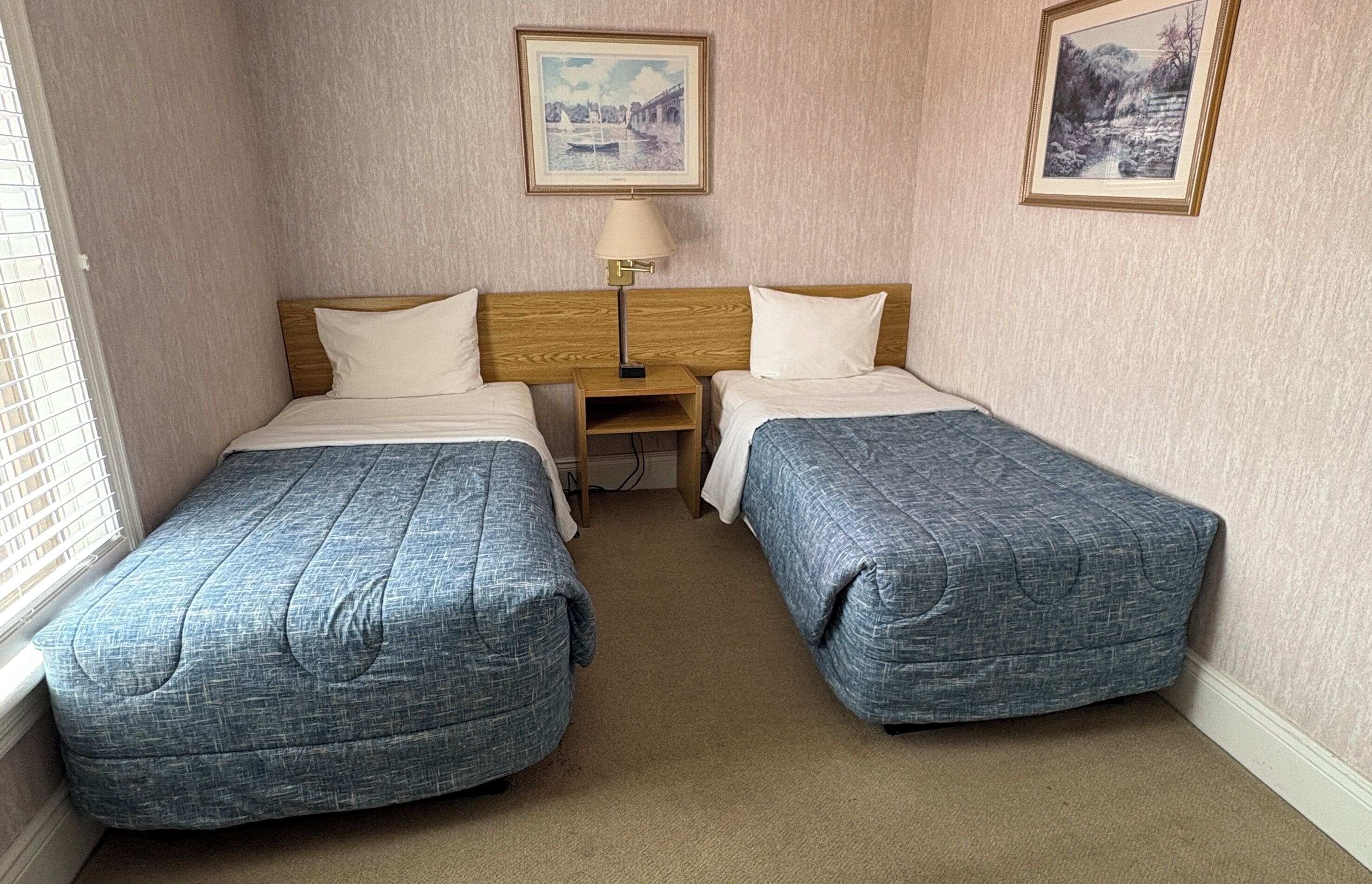 Ein Hotelzimmer mit zwei Betten, einem Nachttisch, einer Lampe und zwei gerahmten Bildern an der Wand.