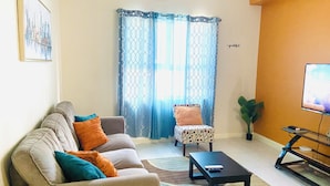 A living room with a sofa, armchairs, a coffee table, a TV, and a plant. - Modern Comfort Suites (Kingston)
