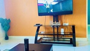 A living room with a flat-screen TV mounted on the wall, a black coffee table, and a glass TV stand with the word "Blessed" on it. - Modern Comfort Suites (Kingston)