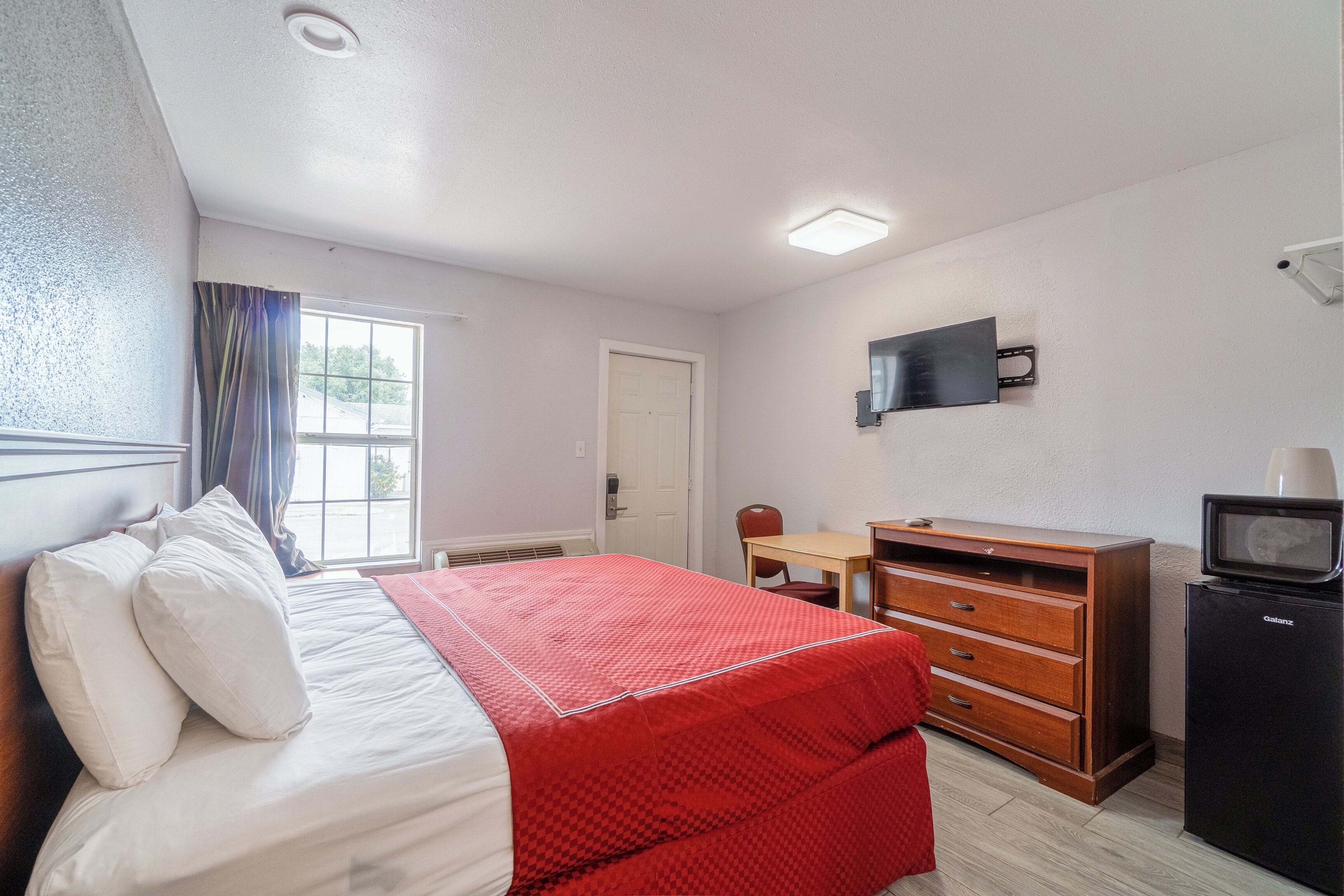Una habitación de hotel con cama, escritorio, cómoda y televisor.