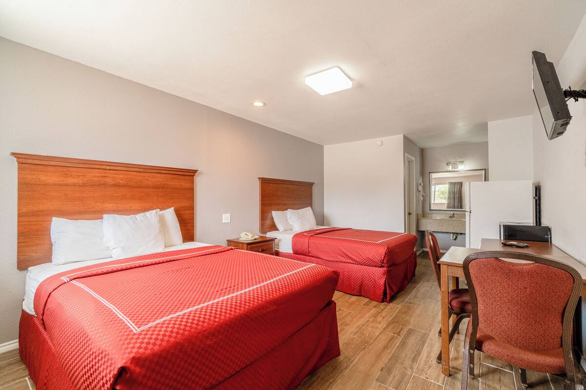 A hotel room with two beds, a desk, a chair, a TV, and a bathroom visible in the background.