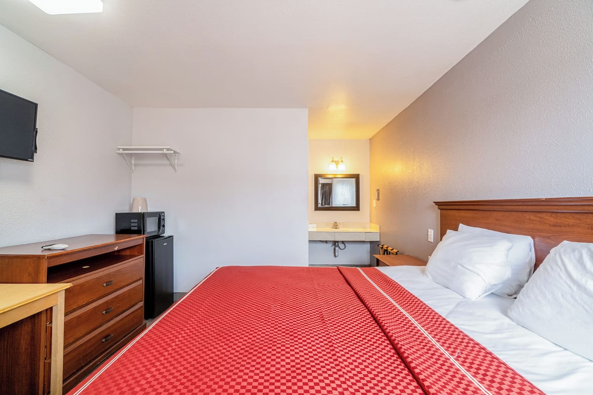 A hotel room with a bed, a desk, a microwave, a refrigerator, a sink, and a mirror.