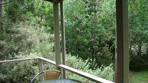 A covered outdoor area with a glass table and wicker chairs, surrounded by dense greenery.
