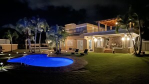 A nighttime view of a two-story house with a swimming pool, outdoor seating, and a covered patio area. - Luquillo Beach- Puerto Rico, 4 Bedroom Vacation Villa With Pool and Wifi (Luquillo)