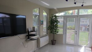 A spacious room with a large flat-screen TV mounted on the wall, a potted plant, and a radiator. - Luquillo Beach- Puerto Rico, 4 Bedroom Vacation Villa With Pool and Wifi (Luquillo)