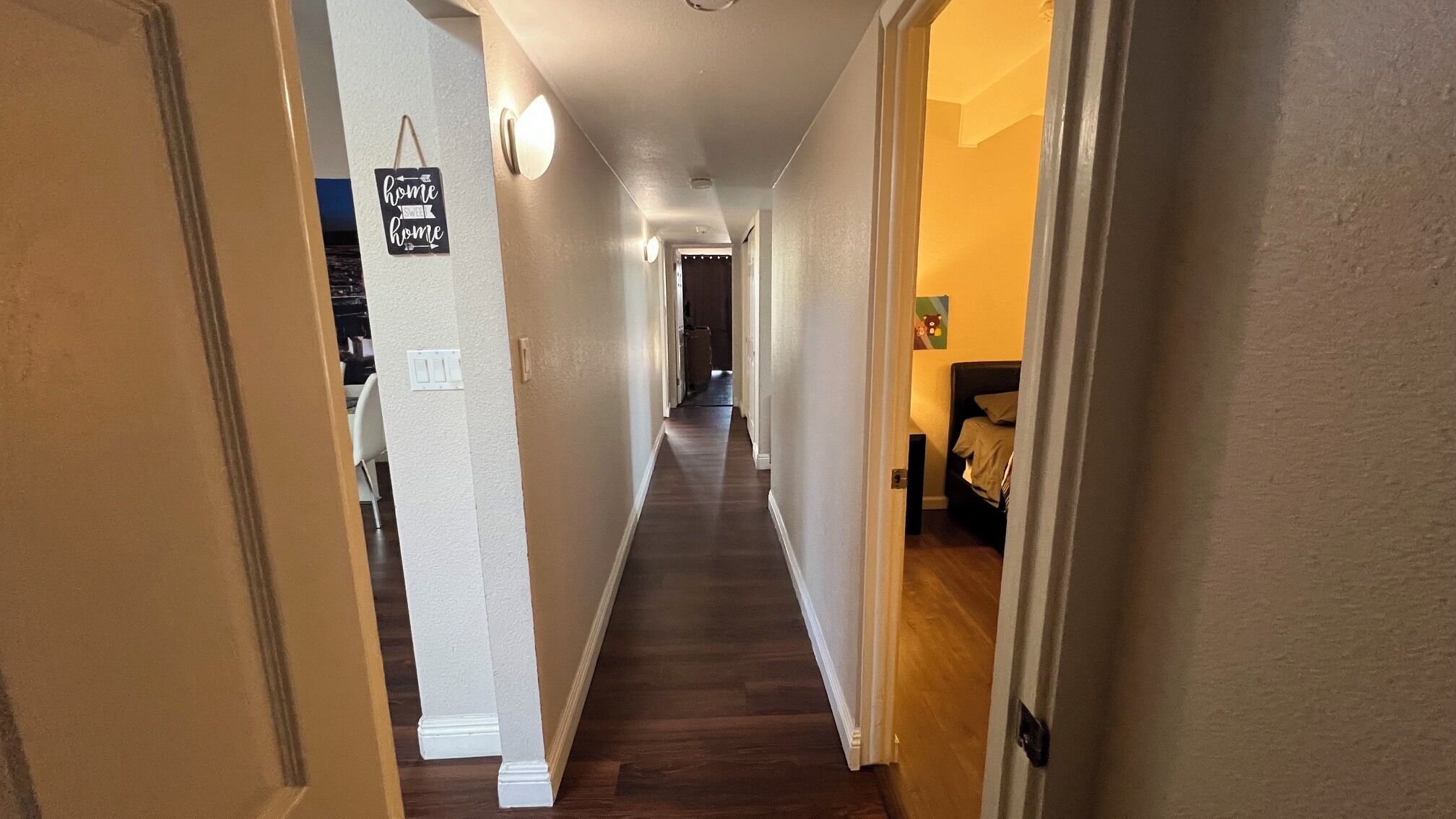 Un couloir avec un plancher en bois, un interrupteur et une pancarte sur laquelle on peut lire : « chez soi, on est bien ».