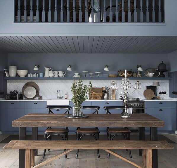 A kitchen with a large wooden table, blue cabinets, and various kitchenware. - Traditional timber house by the sea (Borgarnes)