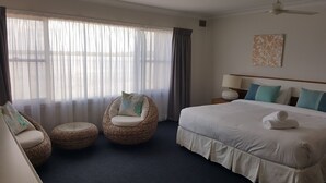 Una habitación de hotel con una cama grande, dos sillas de mimbre, una mesita y un ventilador de techo.