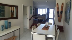 Un área de comedor con una mesa y sillas, una escalera que lleva a un espacio de sala, y esquíes montados en la pared.