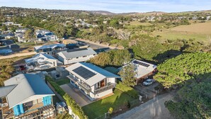 Vista aérea de una zona residencial con casas modernas, algunas con paneles solares, rodeada de vegetación y colinas al fondo.