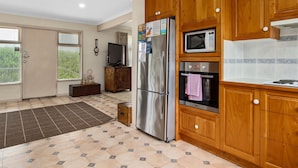 Una cocina con armarios de madera, un refrigerador de acero inoxidable, un microondas, un horno y suelo de baldosas.