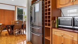 Una cocina con refrigerador de acero inoxidable, microondas, gabinetes de madera y un comedor con mesa y sillas de madera.
