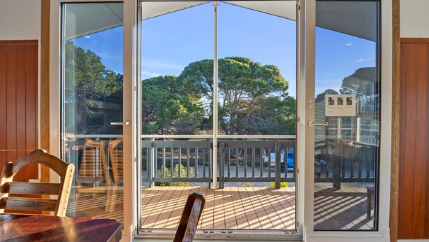 Una habitación con un gran ventanal corredera que da a una terraza exterior con vistas a árboles.