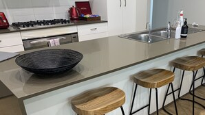 Une cuisine moderne dotée d’un grand îlot central, d’une cuisinière à gaz, d’une machine à café et de trois tabourets de bar en bois.