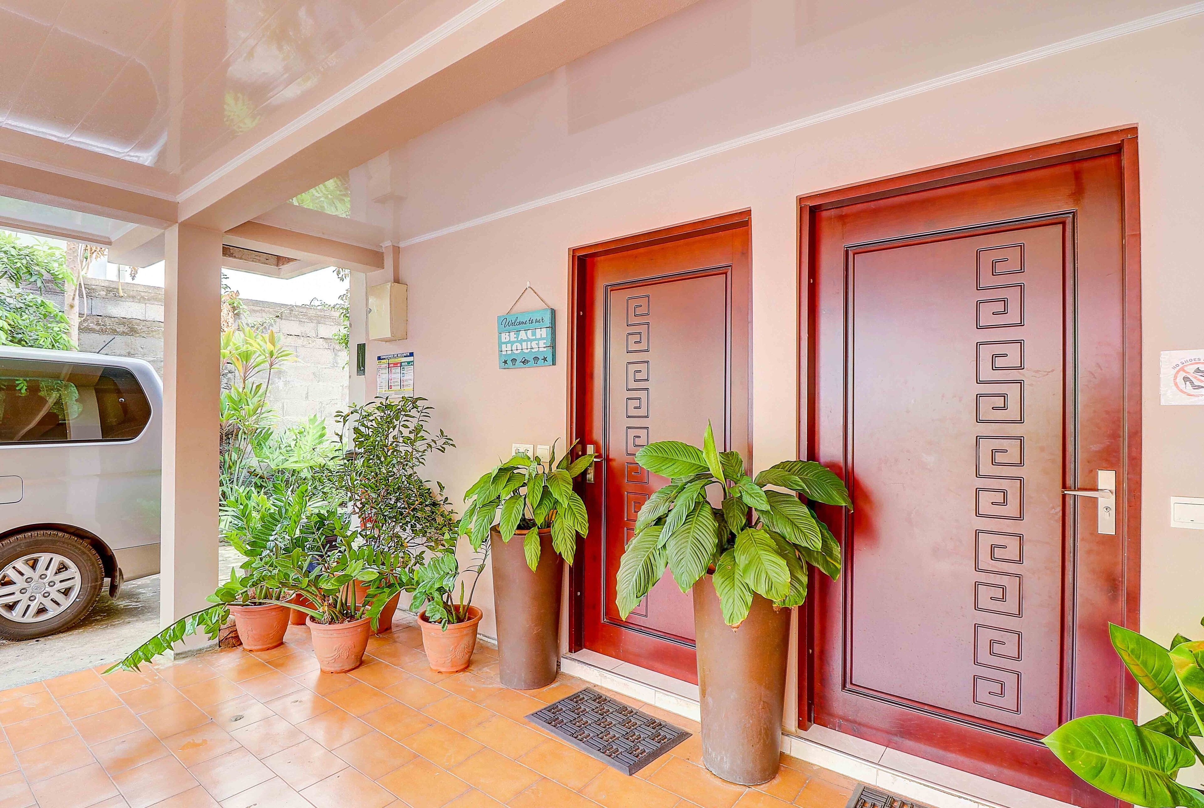 A hotel entrance with two wooden doors, potted plants, and a car parked outside.