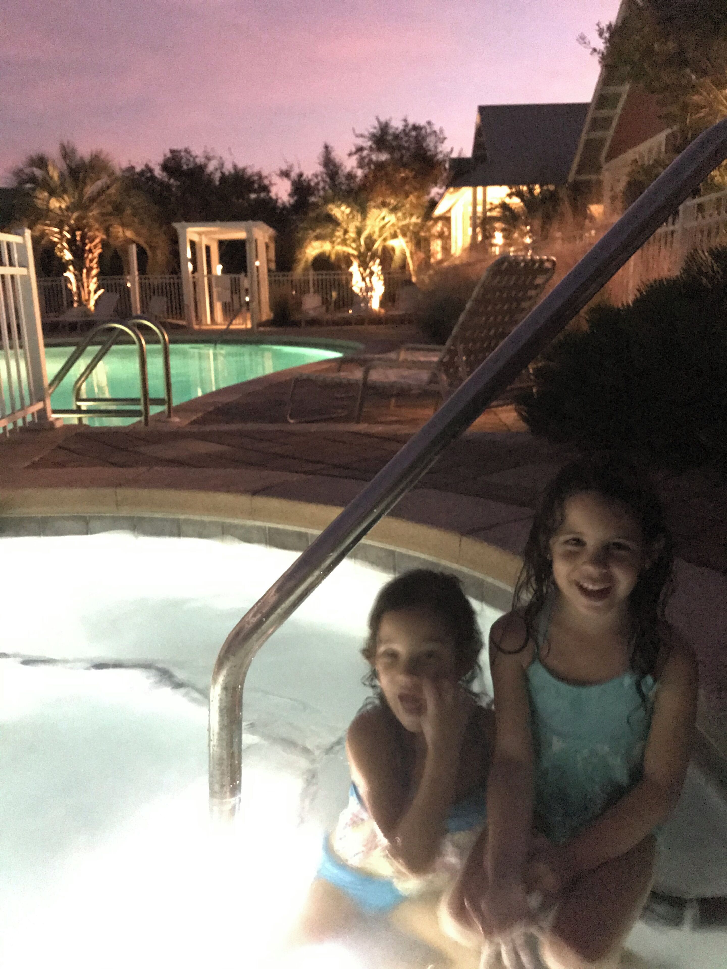 A swimming pool area with a hot tub, a metal ladder, and a poolside seating area.