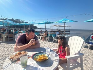 Een restaurant aan het strand met terras, tafels en parasols.