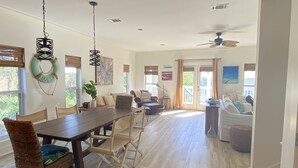 Een ruime woonkamer met een eettafel, stoelen en een plafondventilator.
