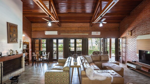A spacious living area with a long sofa, a television, and a fireplace. There are two ceiling fans and a brick wall. - Place with complete leisure 100km from São Paulo (Porto feliz)
