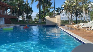 A swimming pool with clear blue water, surrounded by palm trees and a brick building. - Place with complete leisure 100km from São Paulo (Porto feliz)