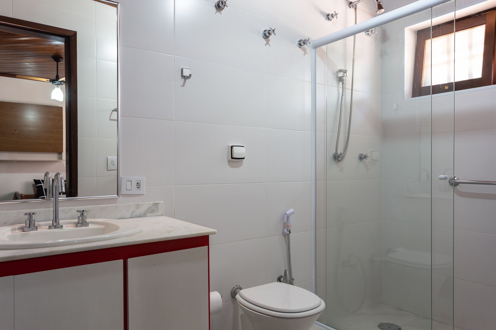 A modern bathroom with a glass shower enclosure, a white sink with two faucets, and a toilet.